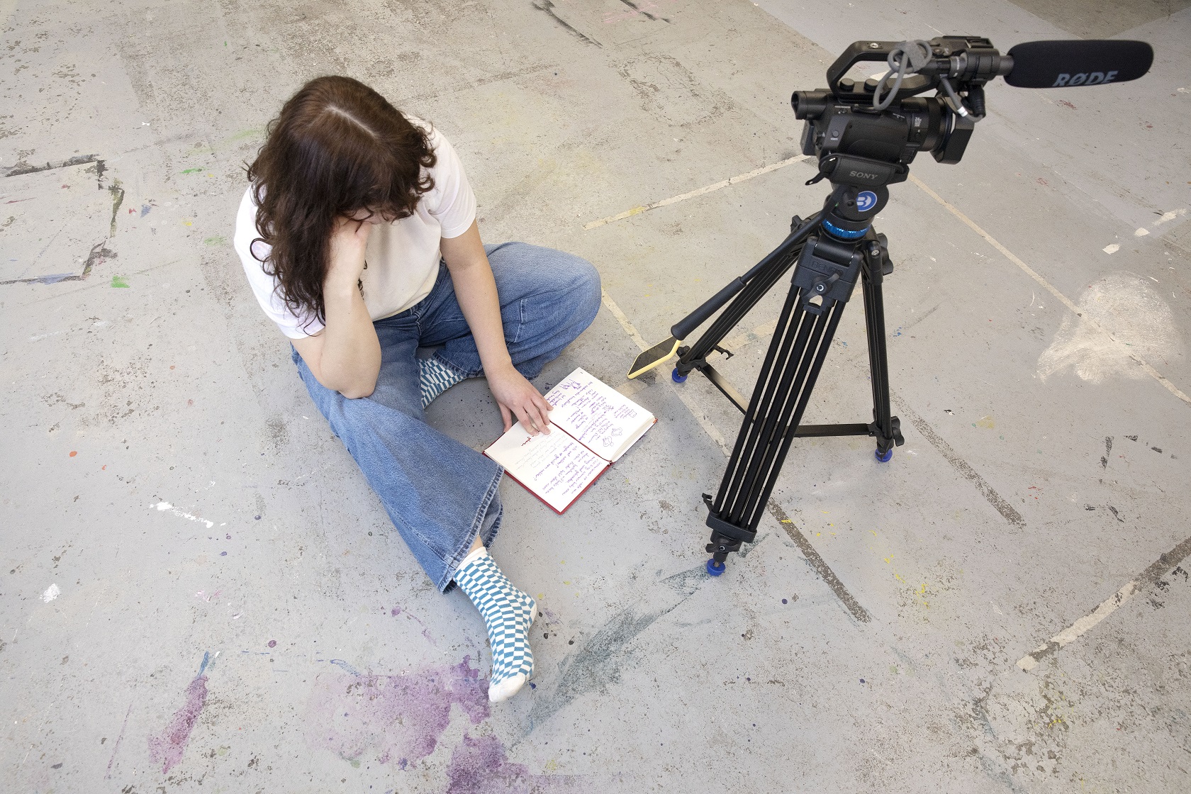 Op de HKU in de Pastoe Fabriek. Foto van bovenaf. Sanne zit op de grond en leest in haar notitieboekje. Daarnaast staat een statief met camera.